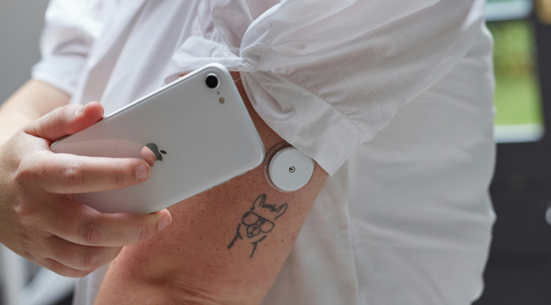 A woman scanning blood glucose with a mobile phone and a flash glucose monitor on her arm.